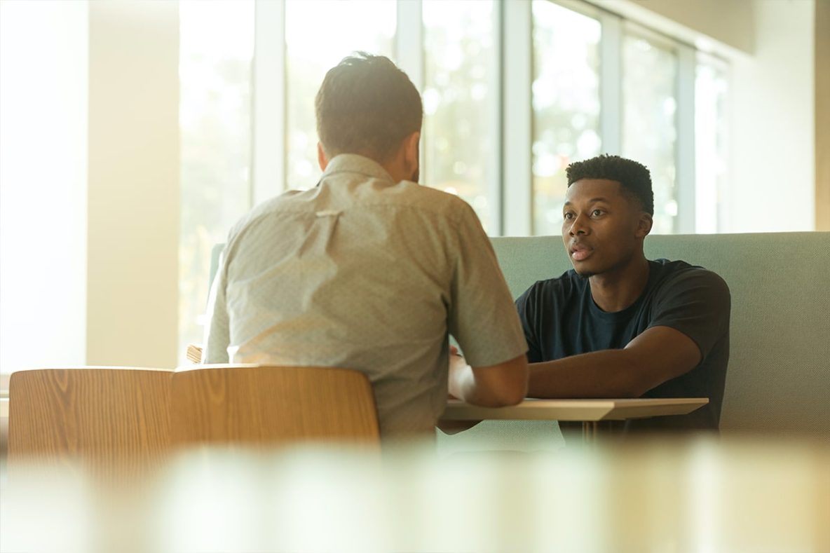 Men speaking at table.