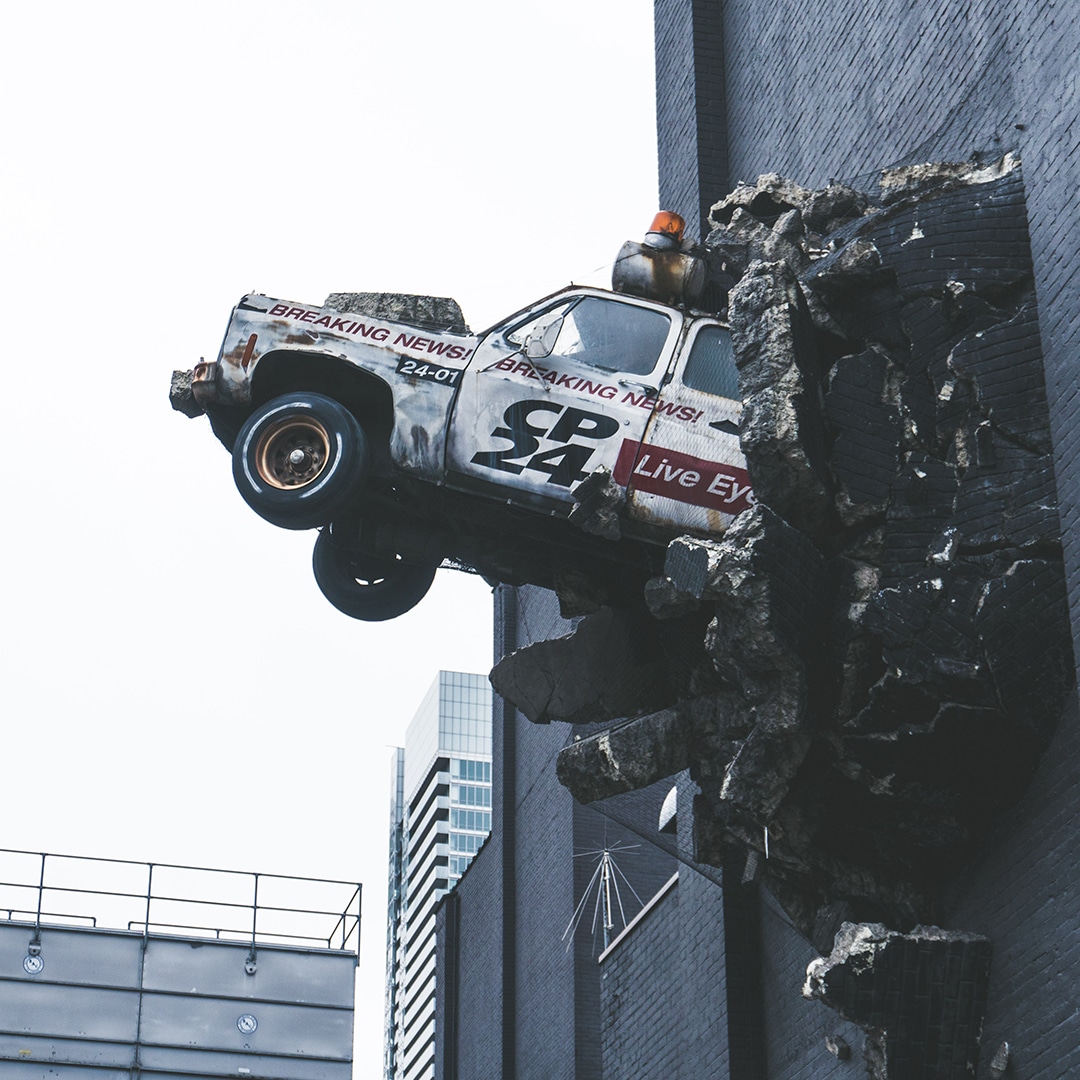 A news truck coming out of the side of a building that's in the air